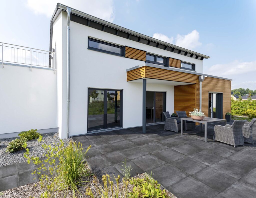 Terrasse mit einer anthrazit farbigen Terrassenfliese. Das Haus ist weiß und hat viel Holzvertäfelung an der Hauswand.