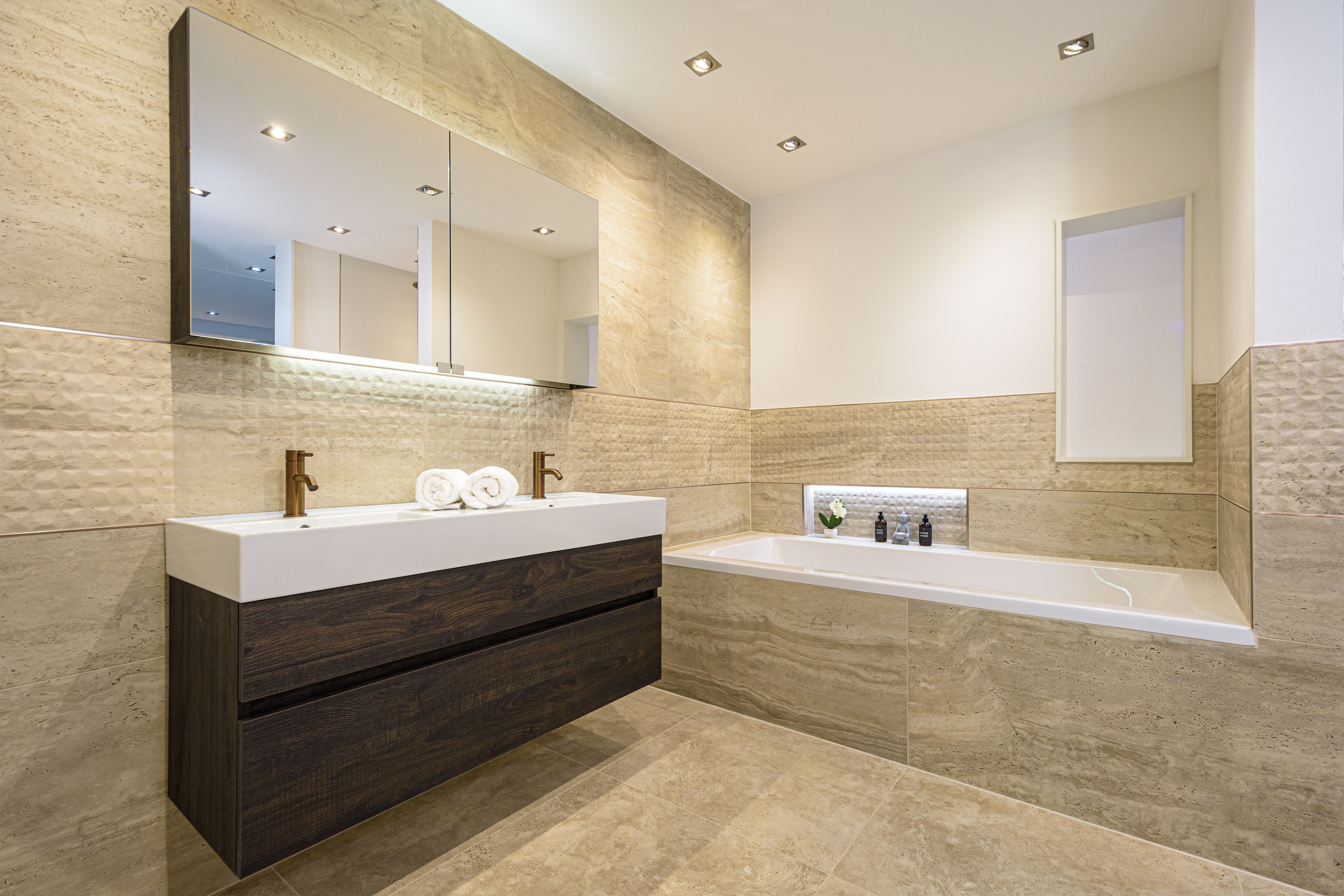Badezimmer in einer Travertinoptik, mit Waschtisch und Badewanne